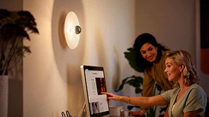 Ženy pracující u počítače vedle nástěnné zrcadlové LED žárovky Philips