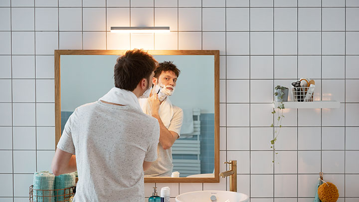 Muž se holí před koupelnovým zrcadlem osvětleným nástěnným LED světlem Philips