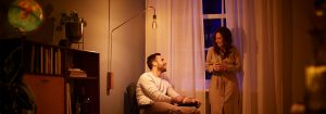 „Stojací lampa s LED žárovkou ve vintage stylu vytváří hřejivou atmosféru pro večerní konverzaci v páru a představuje energeticky úsporné náladové osvětlení v útulném obývacím pokoji.“