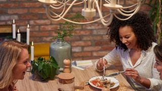 „Moderní kuchyň se závěsnými světly LED ve vintage stylu, která osvětlují dvě ženy při večeři a vytvářejí příjemnou atmosféru.“
