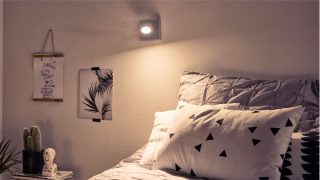 "Stylová ložnice s nastavitelným LED reflektorem vytvářející útulnou atmosféru, osvětlující geometrické povlečení a minimalistický dekor."
