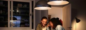 "Moderní LED závěsná svítidla vytvářejí vřelou atmosféru pro dvě ženy, které si užívají konverzaci, a představují energeticky účinná řešení domácího osvětlení."