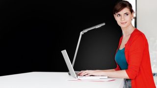 Žena studuje u stolu s nastavitelnou LED lampou, která poskytuje optimální osvětlení pro domácí úkoly v barevném domácím studijním prostoru.